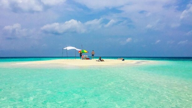 Una playa con agua turquesa cristalina, una orilla arenosa y algunas personas relajándose bajo sombrillas.