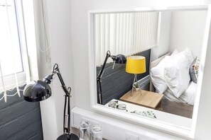 Une chambre d’hôtel avec un lit, une table de chevet avec une lampe, un miroir et une fenêtre avec des stores.