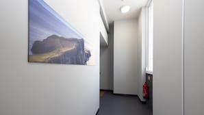 A hallway with a large landscape painting on the wall, a fire extinguisher, and a window on the right.