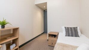 A bedroom with a bed, bedside table, and a shelf with a plant and cups. - JOIVY Meadows Park Ensuite Single Room (Edinburgh)