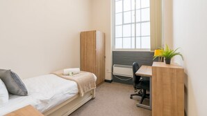 A small, well-lit room with a bed, a desk, a chair, a wardrobe, and a window with blinds. - JOIVY Meadows Park Ensuite Single Room (Edinburgh)