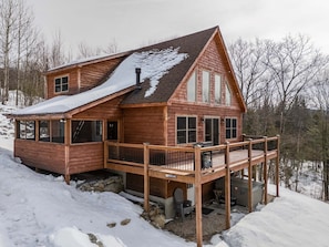 A wooden cabin with a deck, large windows, and a chimney.