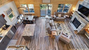 A cozy cabin interior with a dining area, sofa, fireplace, and large windows.