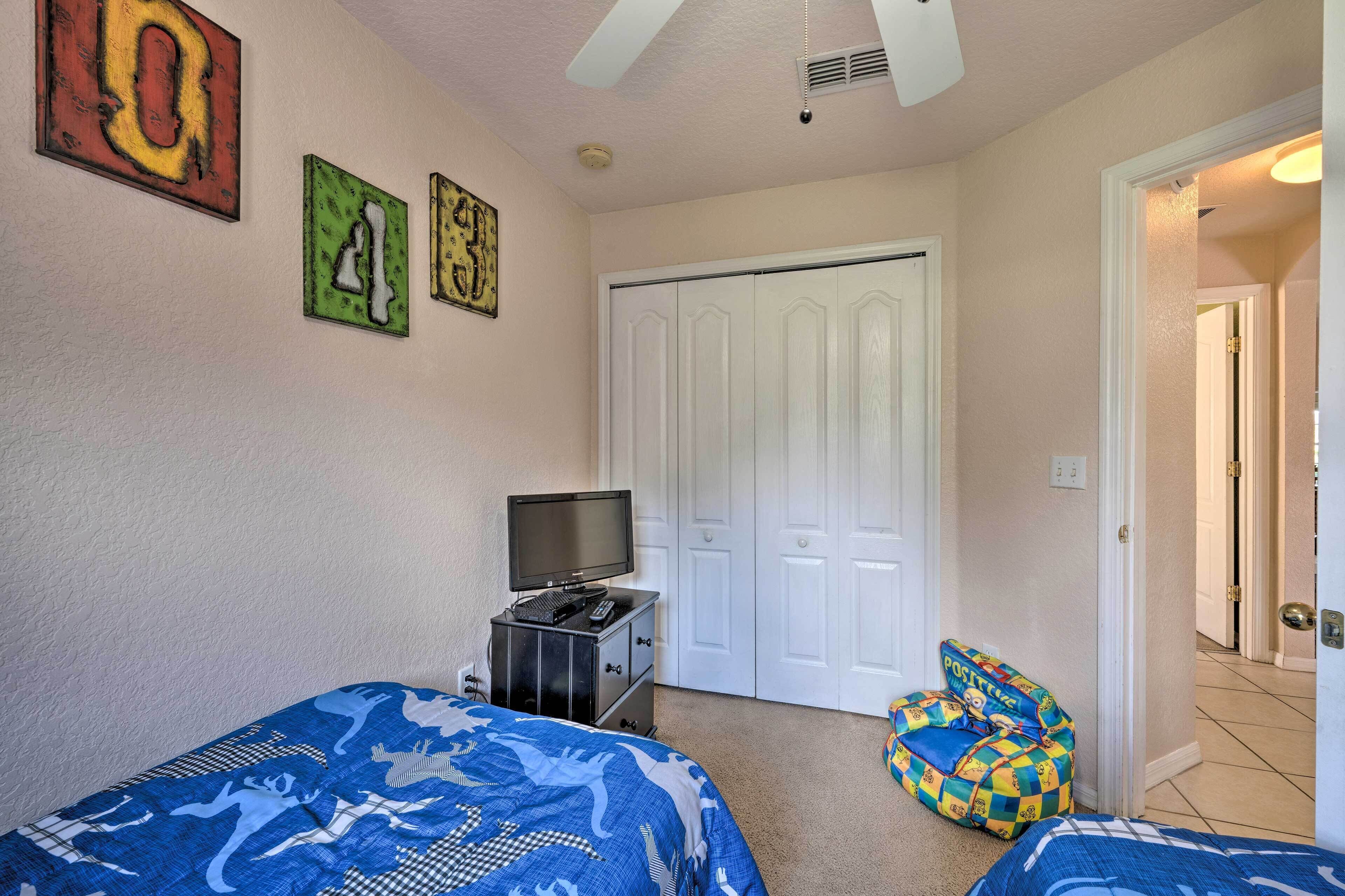 A bedroom with two beds, a TV, and a door leading to another room.