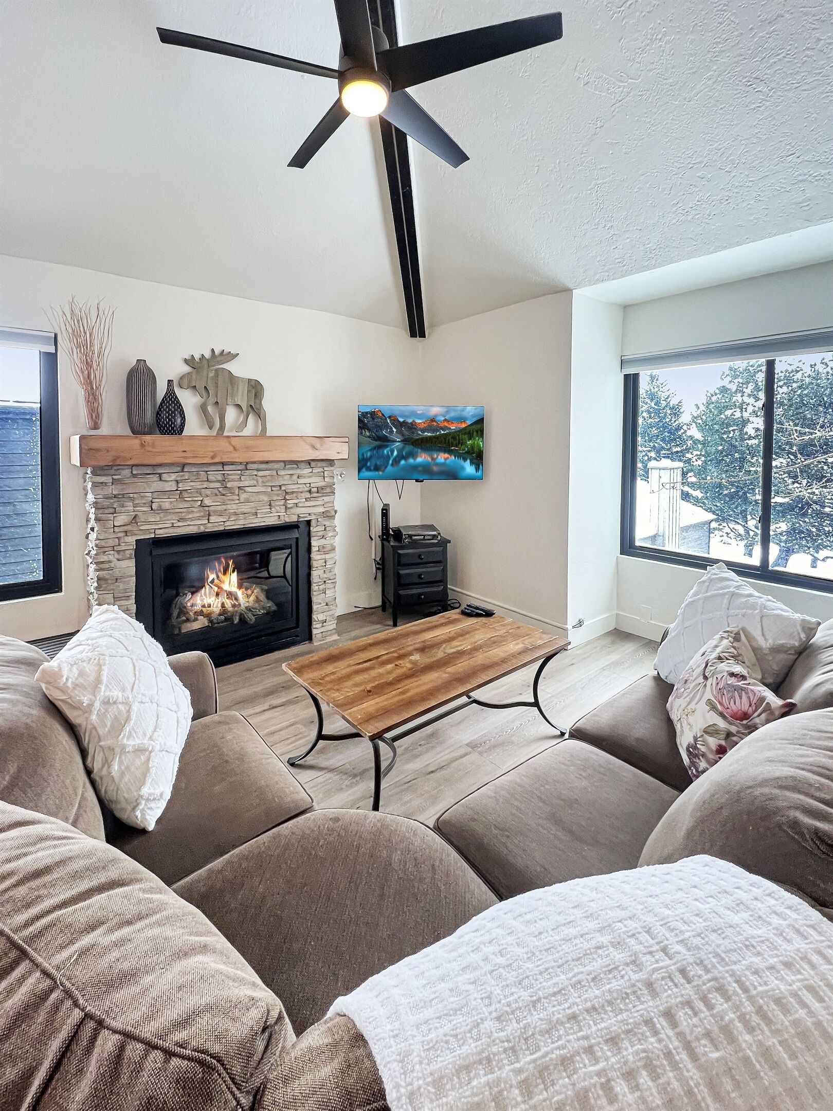 Una sala de estar con chimenea, televisor montado y ventilador de techo.