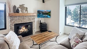 A living room with a fireplace, a mounted TV, and a ceiling fan. - Walk to Ski | Hot Tub | Great Location (Park City)