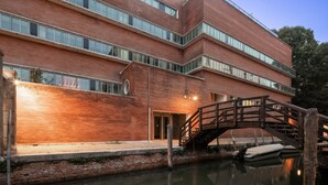 Un edifici de maó de diversos pisos amb un pont de fusta sobre un canal.