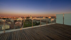 Een houten terras met een glazen balustrade met uitzicht op een stadsgezicht bij zonsondergang.