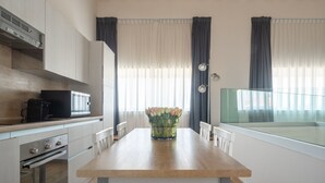 Een moderne keuken met een houten plafond, witte kastjes, een inbouwoven en een eettafel met een bloemetjesvaas.
