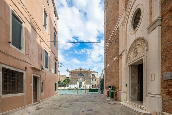 A narrow street with buildings on either side, a canal in the center, and a church in the background. - Bright Apartment On Venetian Roofs R&R (Santa Croce)