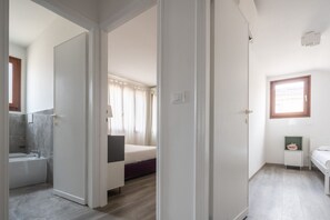 A hotel room with a bathroom, a bed, a small table, and a window. - Bright Apartment On Venetian Roofs R&R (Santa Croce)