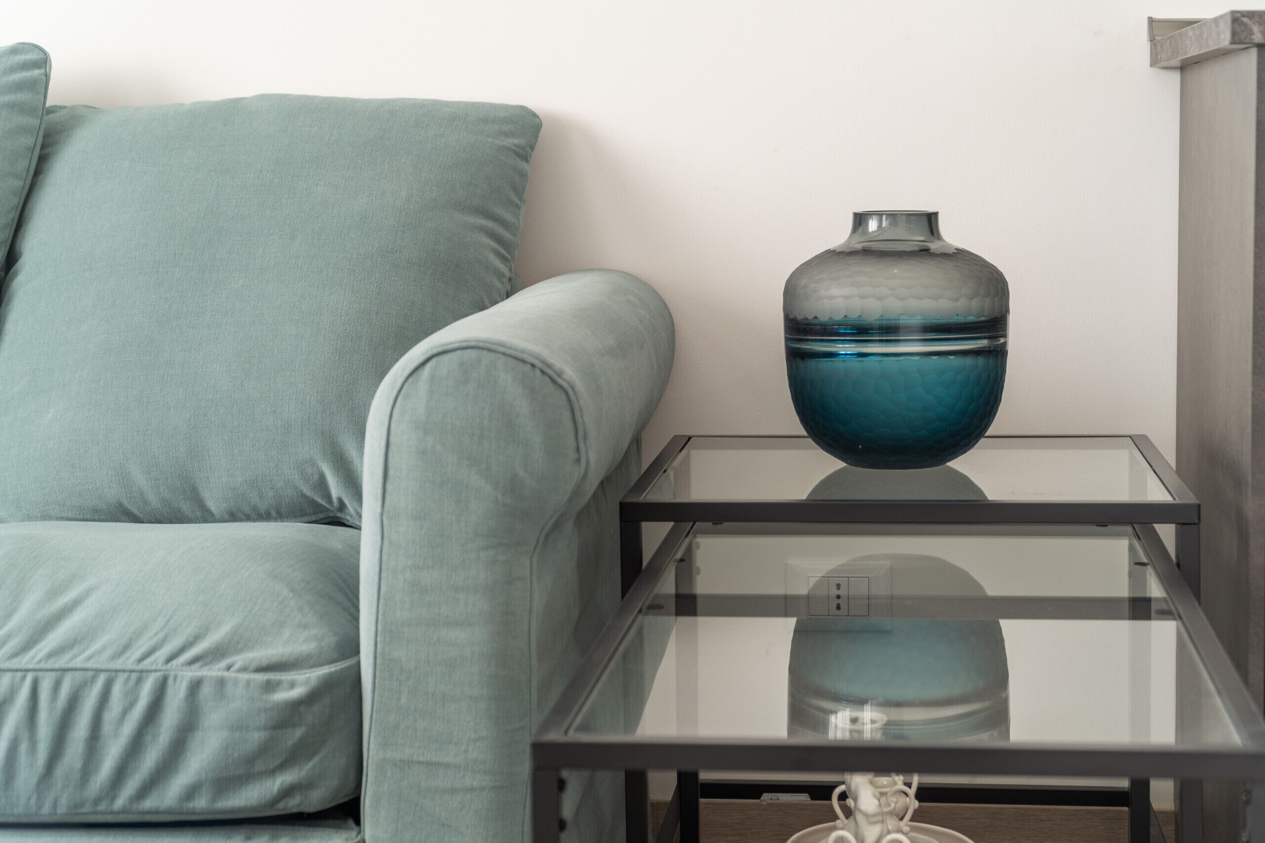 Un salon moderne avec un canapé vert clair, une table basse en verre et un vase décoratif.