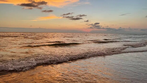 Een strand met golven en een zonsondergang.