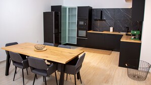 A compact kitchen with a wooden dining table, chairs, and modern appliances including a refrigerator, oven, and coffee machine. - Beautiful 3-bed Villa in Preveza (Preveza)