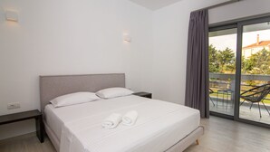 A hotel room with a bed, a nightstand, a window with curtains, and a view of the outdoors. - Beautiful 3-bed Villa in Preveza (Preveza)