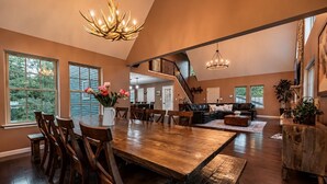 A spacious living area with a large wooden dining table, multiple seating options, and a staircase leading to an upper level. - The Fawn Château w/ Game Room & sauna  (Lake Ariel)