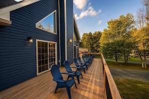 A deck with chairs and a wooden railing, overlooking a grassy area with trees.