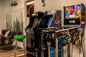 A room with arcade games, including a Spider-Man themed machine, and a bar area with stools.