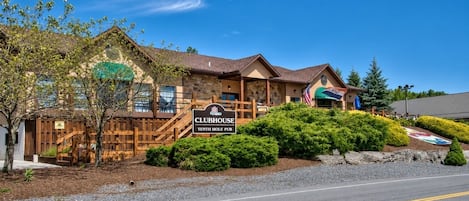 Un pub del hoyo diez del Clubhouse, con fachada de piedra, terraza de madera y jardín ajardinado.