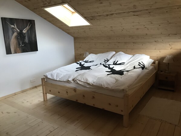 A wooden bed with a white bedspread featuring black deer silhouettes, a painting of a deer on the wall, and a skylight above. - At FOLLO: “Formidable Mayen” made from reclaimed wood (Mase)