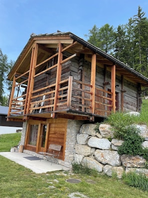 A log cabin with a stone foundation, wooden balcony, and a stone wall surrounding the property. - At FOLLO: “Formidable Mayen” made from reclaimed wood (Mase)