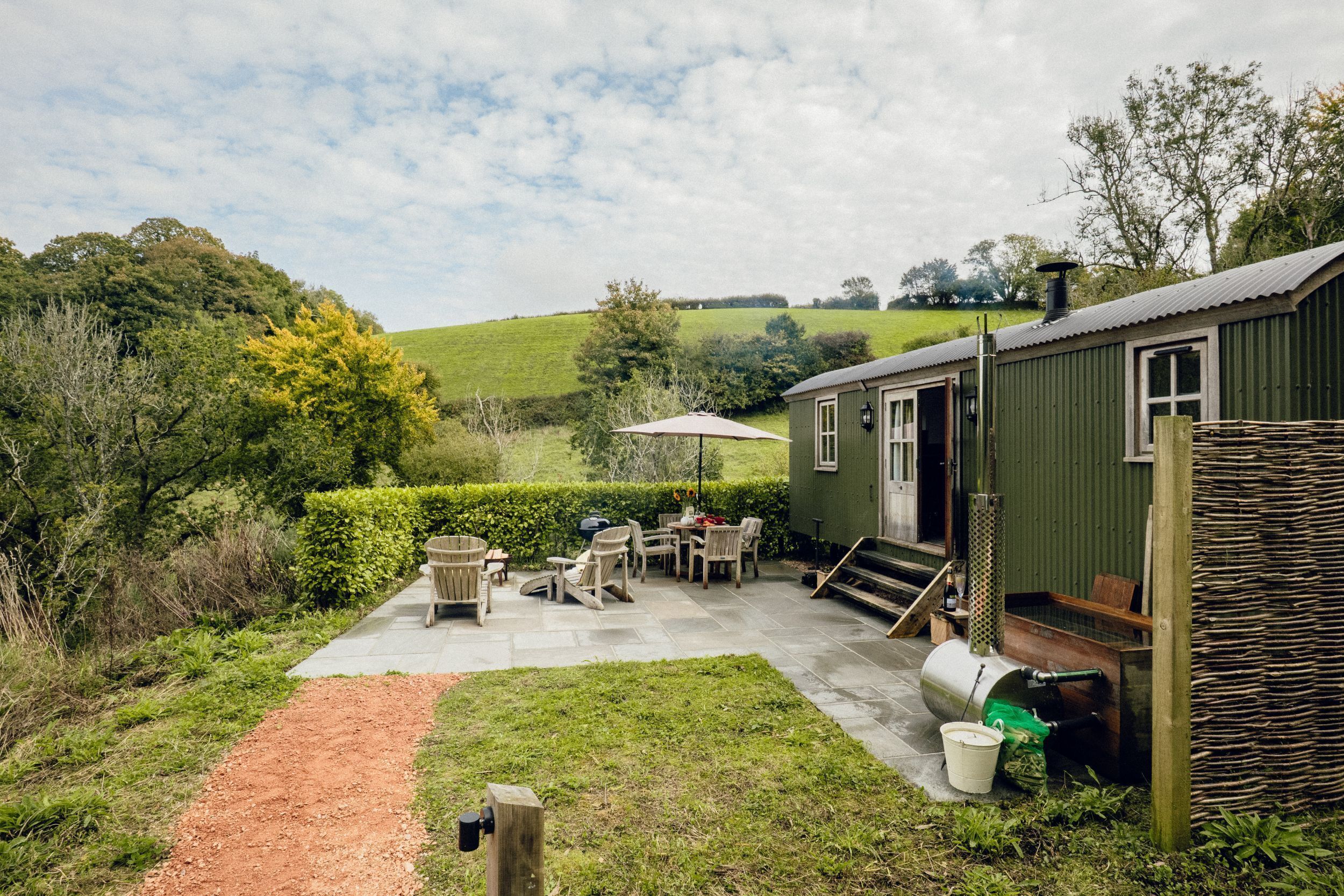 A green building with a patio area, outdoor furniture, and a path leading to the entrance.