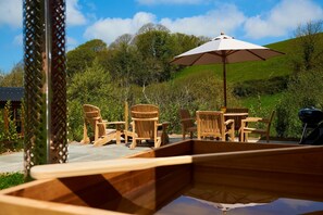 An outdoor seating area with wooden chairs and a table, an umbrella, and a grill.