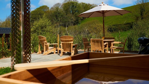 An outdoor seating area with wooden chairs and a table, an umbrella, and a grill. - Oak Shepherds Lodge -  Sleeps 2 (Dittisham)