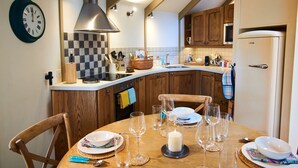 A kitchen with wooden cabinets, a built-in stove, and a dining area with a table set for four. - Buzzard Treehouse -  a dittisham  that sleeps 5 guests  in 1 bedroom (Dittisham)
