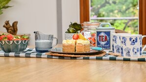 A breakfast setting with a bowl of strawberries, a glass pitcher, a jar of tea, and a mug with dog faces. - Buzzard Treehouse -  a dittisham  that sleeps 5 guests  in 1 bedroom (Dittisham)