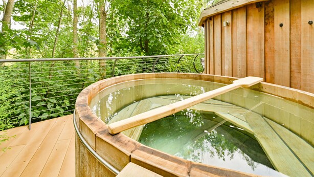 A hot spring bath area with a wooden deck and a wooden building in the background. - Buzzard Treehouse -  a dittisham  that sleeps 5 guests  in 1 bedroom (Dittisham)