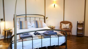 Habitación con una cama individual de estructura metálica, dos mesitas de noche, una silla y una estantería con objetos.