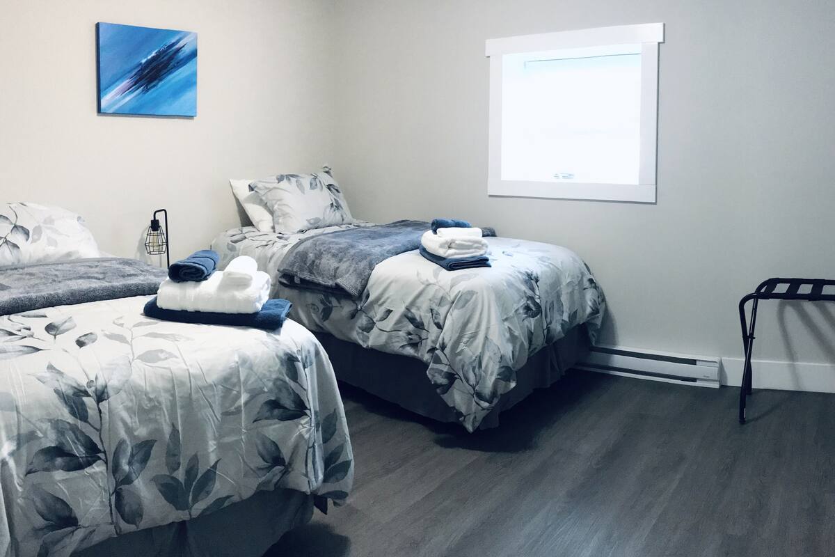 A bedroom with two beds, a window, a radiator, and a wall-mounted artwork.