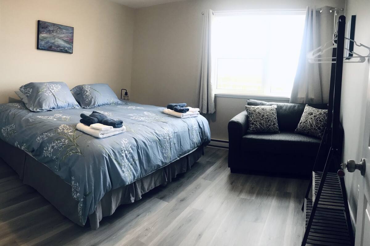 A bedroom with a bed, a sofa, a window, and a painting on the wall.