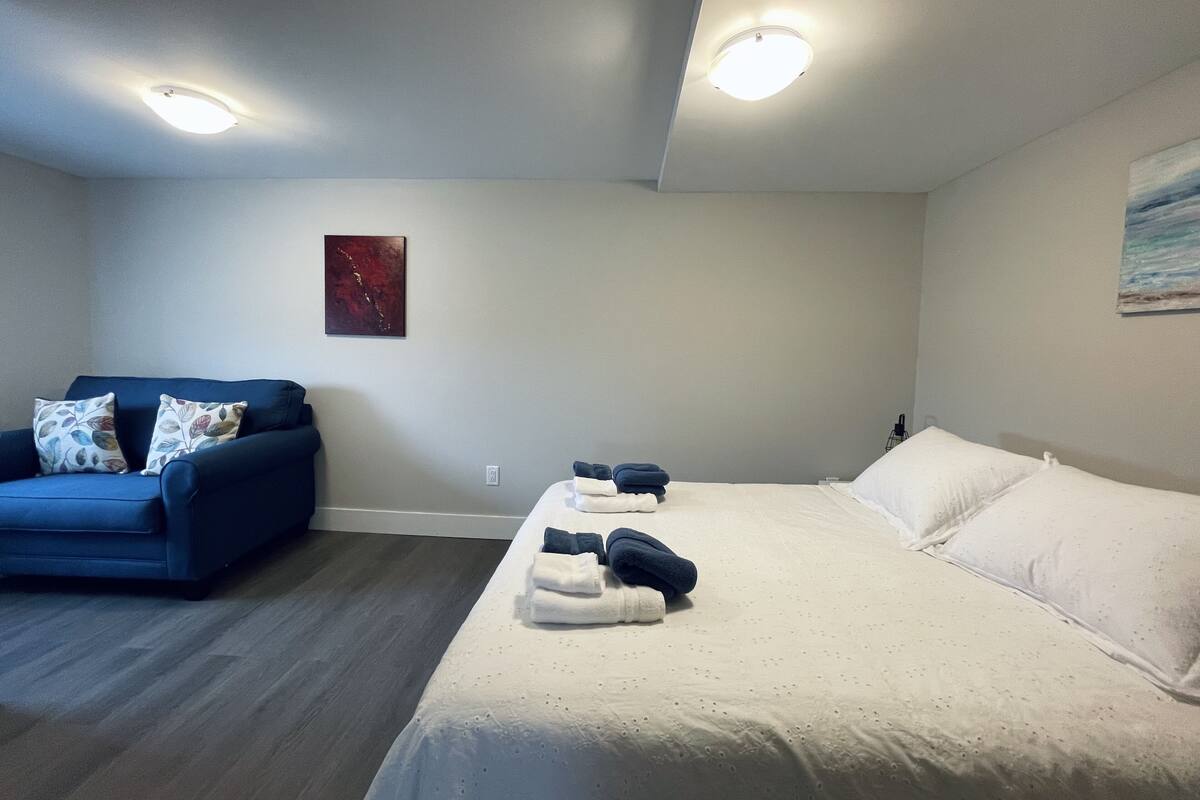 A bedroom with a bed, a blue sofa, and a painting on the wall.