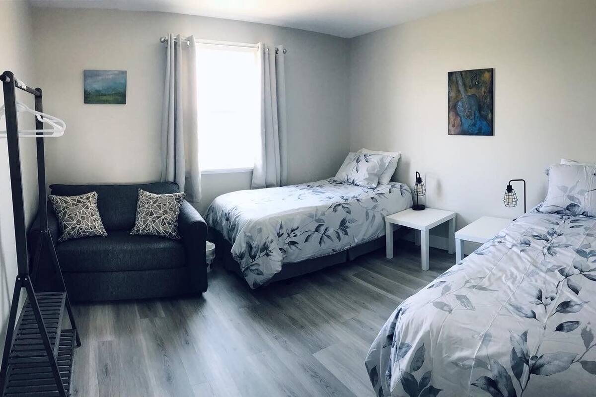 A bedroom with two beds, a sofa, a small table, and a hanging rack.
