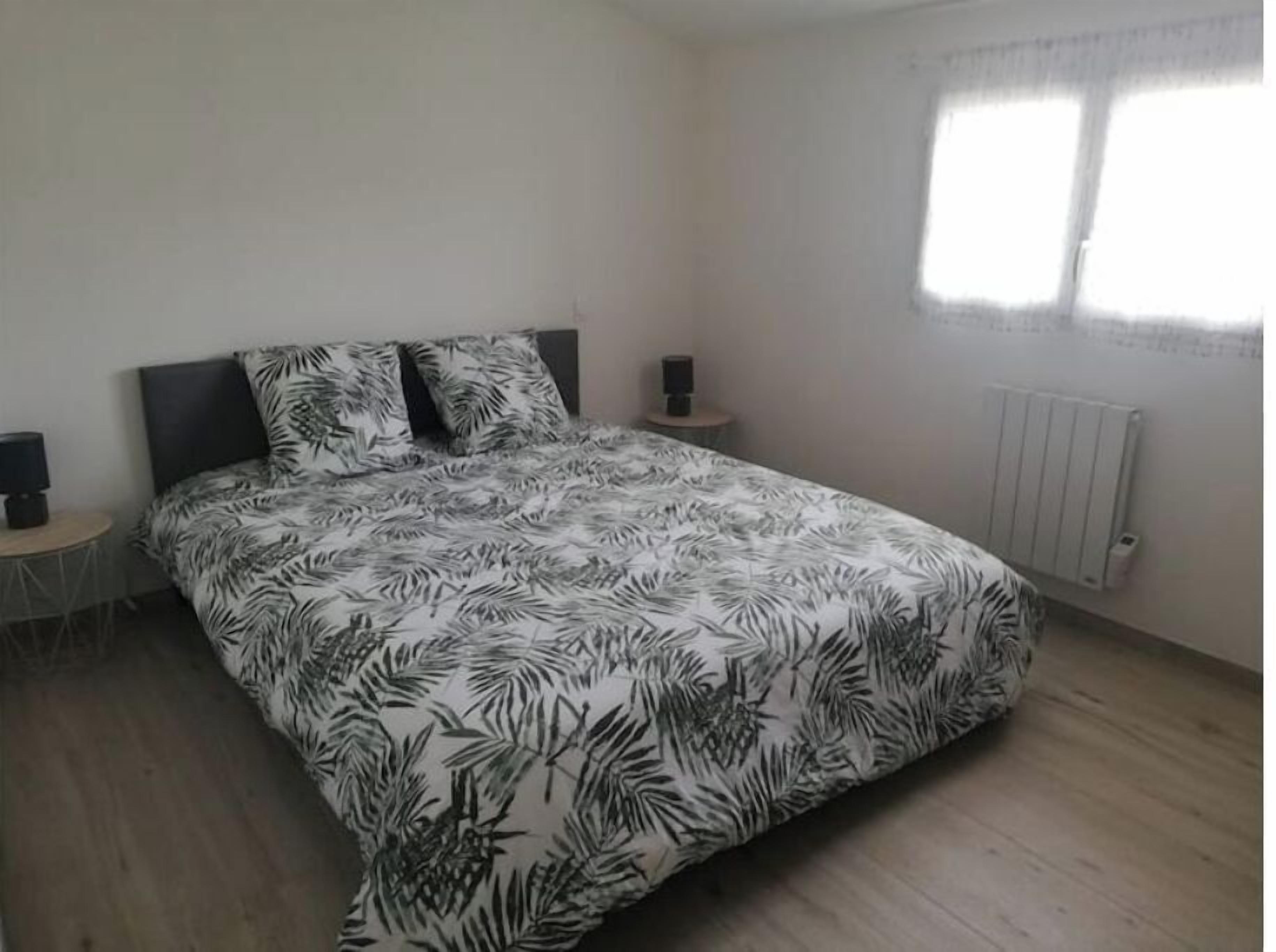 A bedroom with a bed, a nightstand, a radiator, and a window.