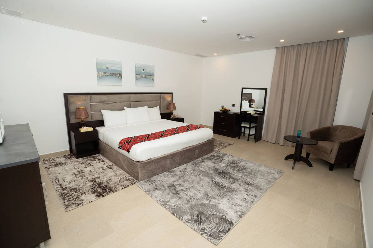 A modern hotel room with a large bed, a desk, a chair, and a mirror.