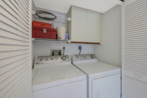 A laundry room with two white washing machines, a red toolbox, and a white cabinet above. - Rare Riverfront Condo | Pool, Spa, & Tennis Court (Marco Island)
