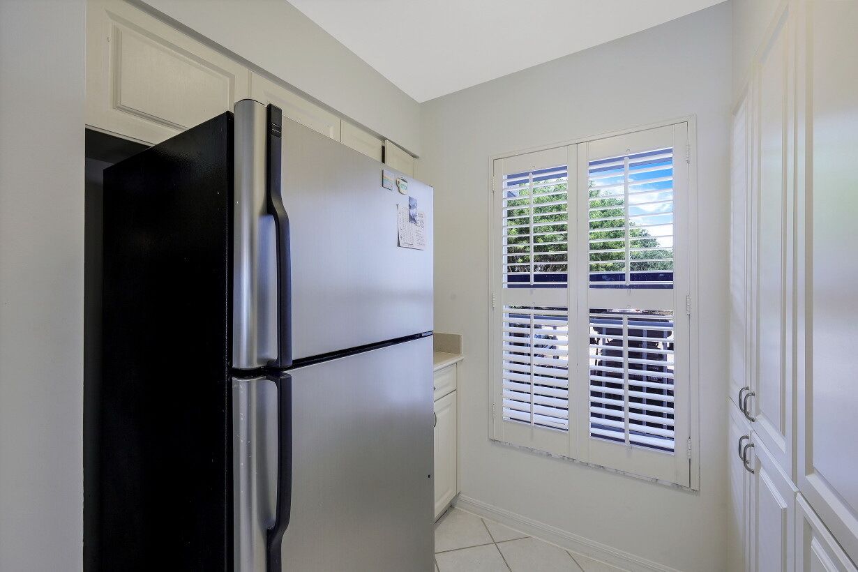 A kitchen with a black refrigerator, white cabinets, and a window with blinds.