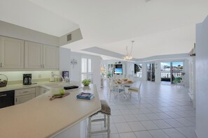 A spacious kitchen with a large island, white cabinetry, and a view to a balcony. - Rare Riverfront Condo | Pool, Spa, & Tennis Court (Marco Island)