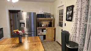 A compact kitchen with a refrigerator, microwave, oven, and a small coffee maker on a shelf. There's a trash bin and a radiator on the floor. - Finger Lakes Escape: Spacious 5-Bedroom Home in Canandaigua (Canandaigua)