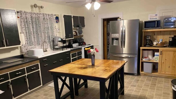 A compact kitchen with a wooden table, black cabinets, a refrigerator, a microwave, and a ceiling fan. - Finger Lakes Escape: Spacious 5-Bedroom Home in Canandaigua (Canandaigua)
