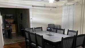 A dining area with a rectangular table surrounded by six chairs, a ceiling fan, and a kitchen in the background. - Finger Lakes Escape: Spacious 5-Bedroom Home in Canandaigua (Canandaigua)