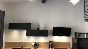 Moderni keittiö, jossa on puinen työtaso, mustat kaapit, musta jääkaappi, mikroaaltouuni, kahvinkeitin ja kaksi riippuvalaisinta.
