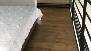 Makuuhuone, jossa on sänky, puulattia, musta kaide ja valkoinen seinä.
