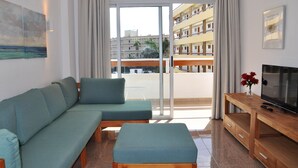A modern living room with a sofa, ottoman, and a TV on a wooden stand.