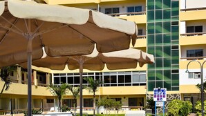 A pool area with lounge chairs and umbrellas, a fountain, and a building with multiple balconies.