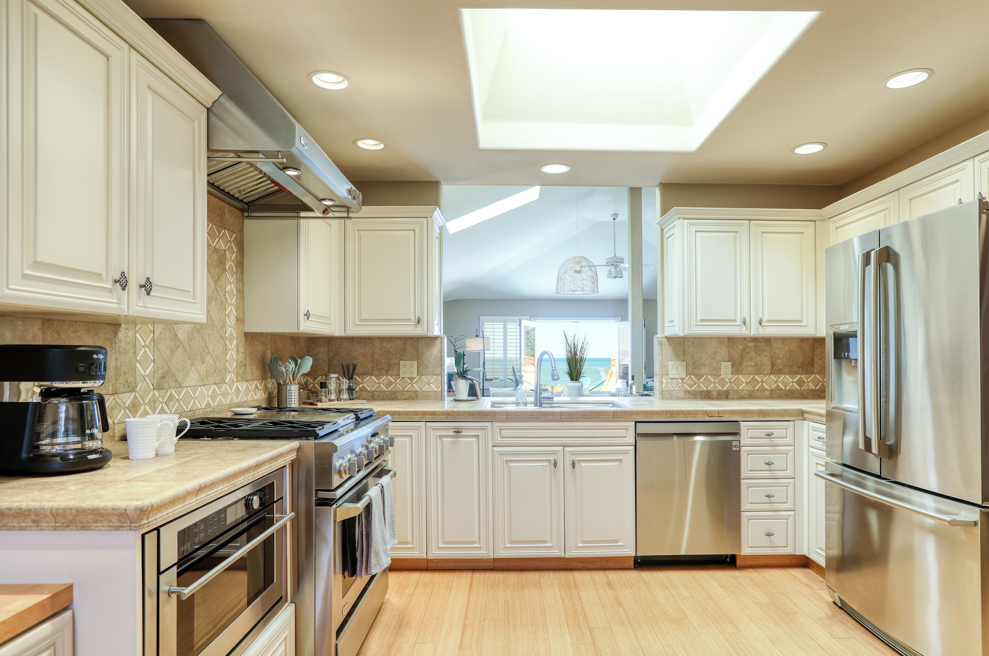 A modern kitchen with white cabinets, stainless steel appliances, a skylight, and a view to the outdoors.