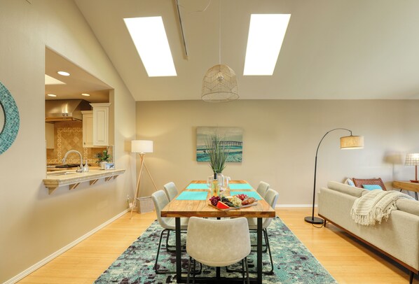 A dining area with a wooden table, chairs, a vase with flowers, and a painting on the wall. - Ebb Tide Luxury Condo in Shell Beach (Pismo Beach)